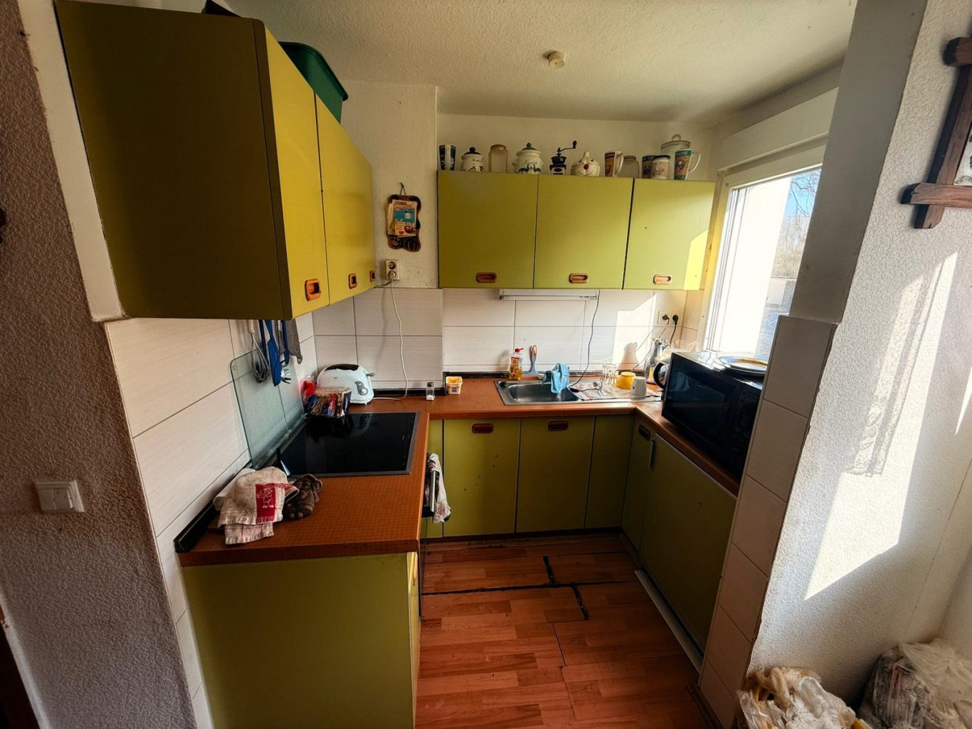 Vorher Küche Haushaltsauflösung Kleine Küche mit grünen Schränken, Holzarbeitsplatte und Fenster mit Tageslicht.