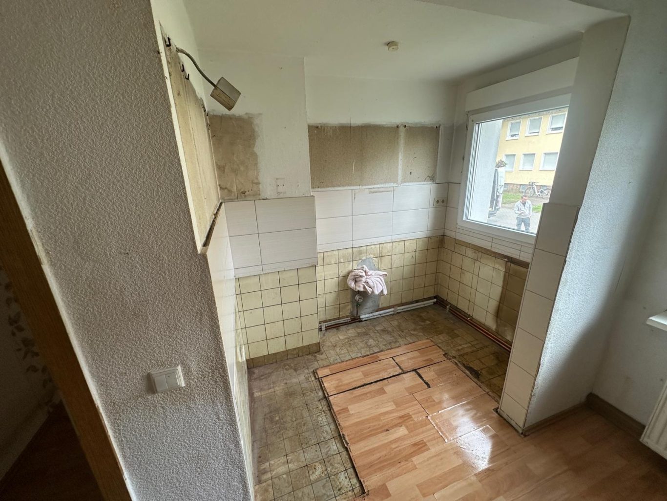 Nachher Bild Küche Wohnungsauflösung Leere Küche mit unvollständiger Wand- und Bodenverkleidung, Fenster und Wasseranschluss sichtbar.