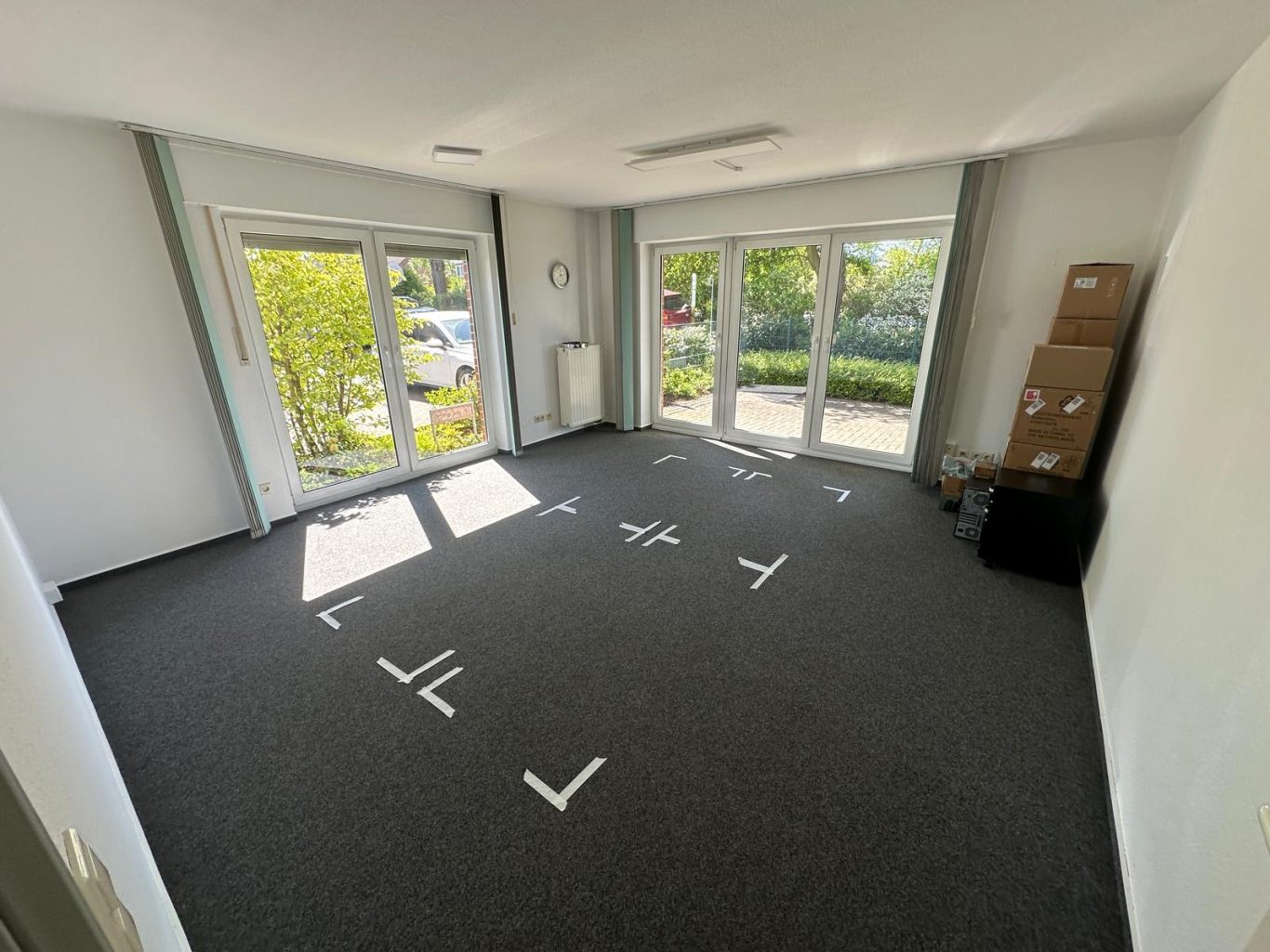 Vorher Bild Büro Umzug Leeres Zimmer mit Teppichboden, großen Fenstern und Umrissen auf dem Boden.
