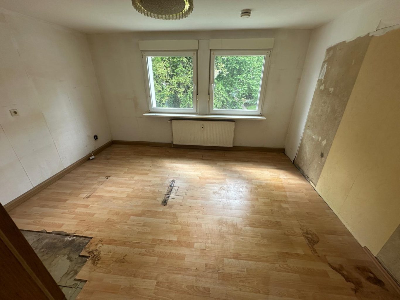 Nachher Bild Wohnungsauflösung Leerer, unrenovierter Raum mit Holzfußboden und Fensterblick auf Bäume.