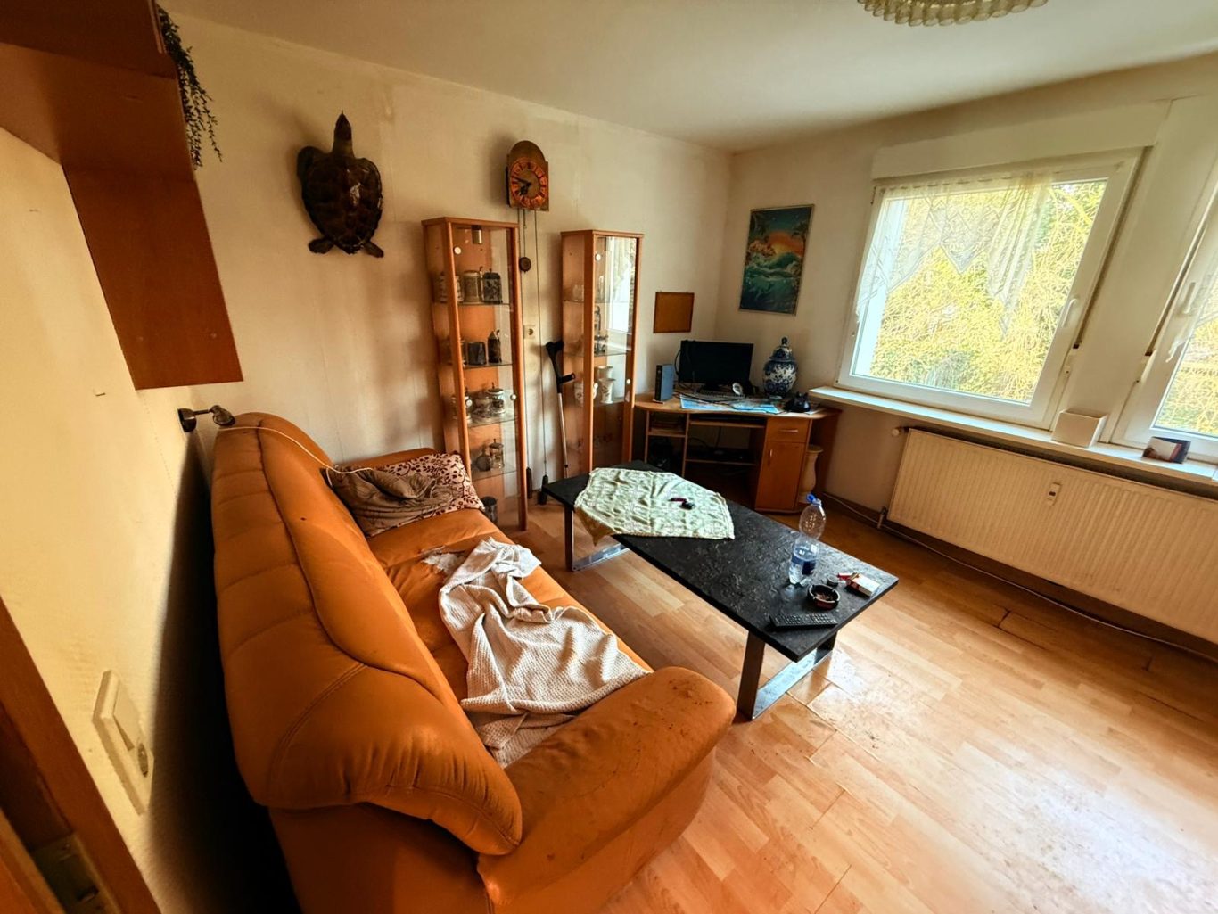 Vorher Bild Wohnzimmer Wohnungsauflösung Wohnzimmer mit orangefarbenem Sofa, Glastisch und Computer auf einem Schreibtisch.