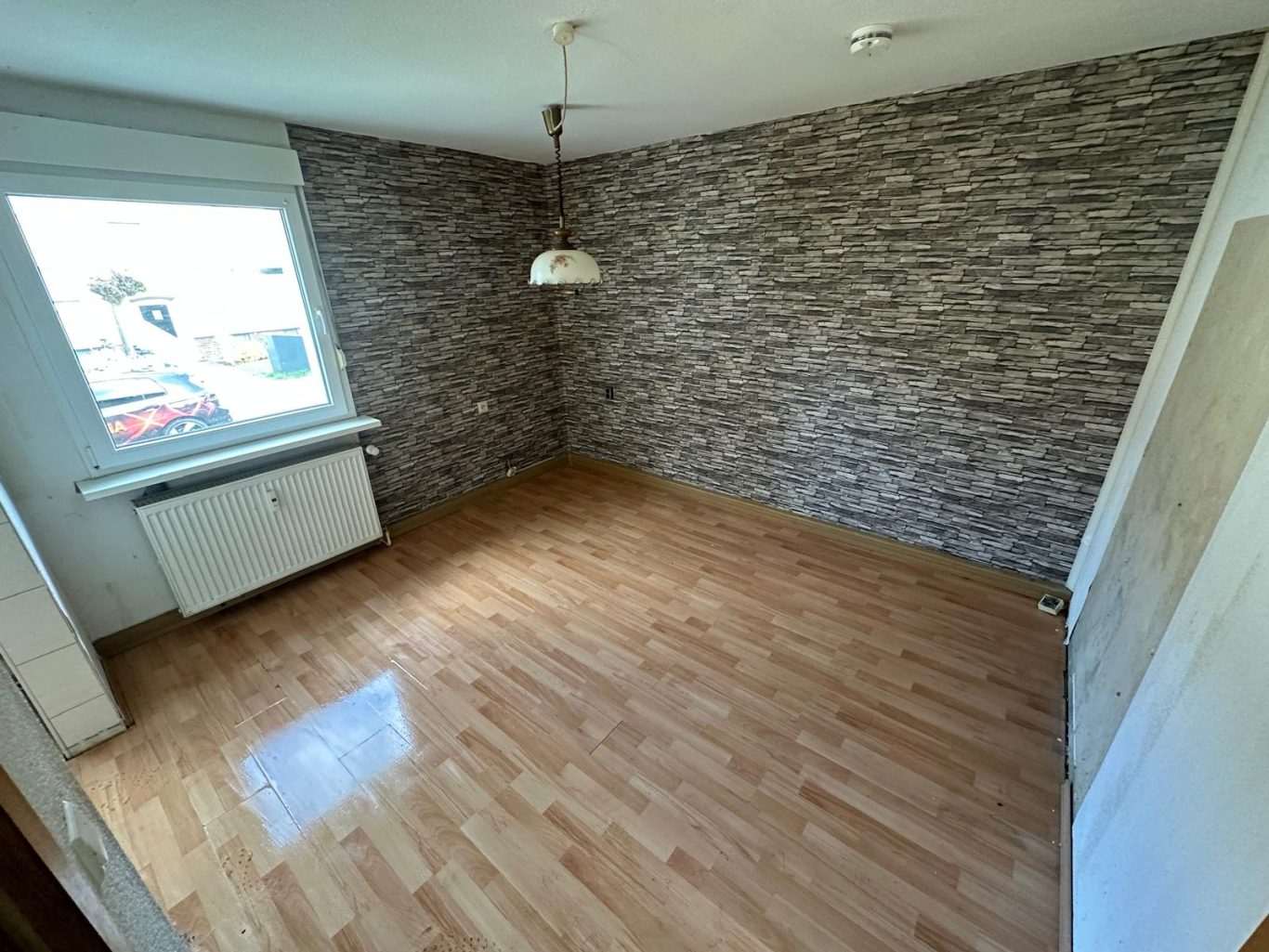 Nachher Bild Esszimmer Wohnungsauflösung Leerer Raum mit Parkettboden und einer Fensterfront, verzierte Wand im Hintergrund.