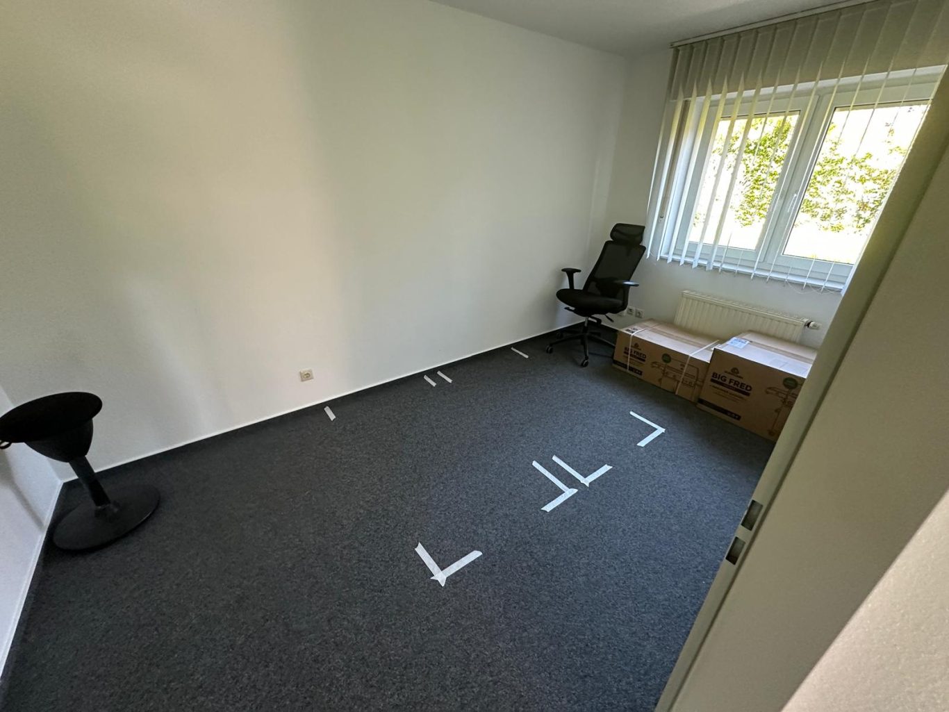 Vorher Bild Büroumzug Leerer Raum mit Teppich, Stuhl, Tisch und Fenstern mit Blick ins Freie.