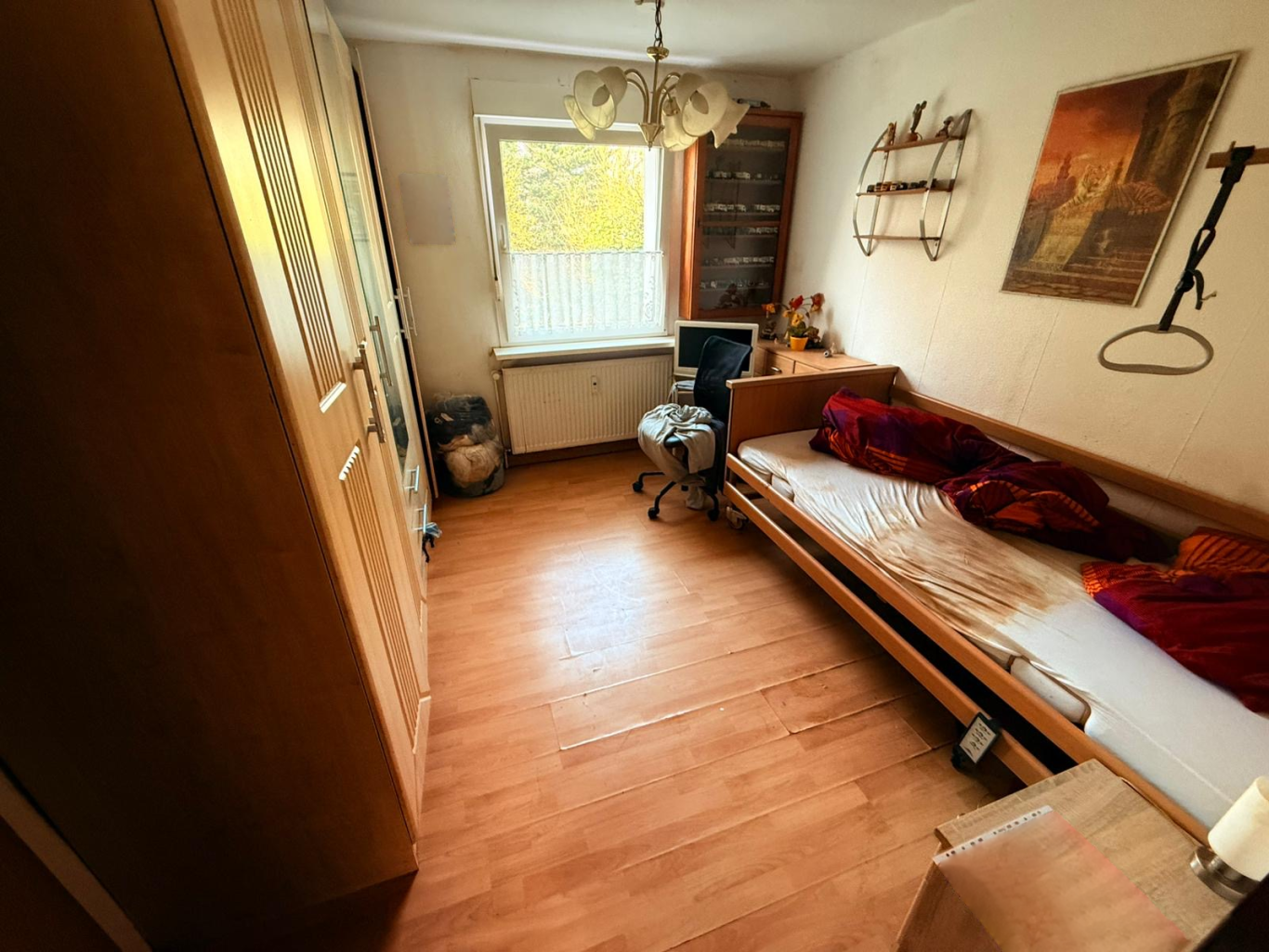 Vorher Schlafzimmer Wohnungsauflösung Kleine, helle Schlafzimmer mit einem Bett, Stuhl und Holzfußboden.