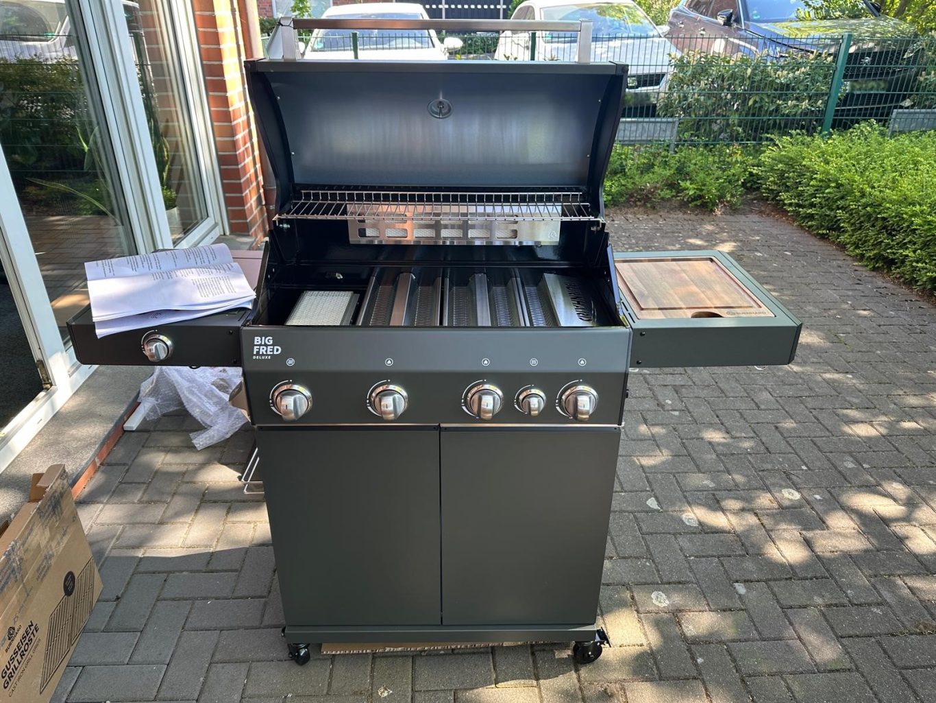 Zusammengebauter Gasgrill Schwarzer Gasgrill mit geöffnetem Deckel und seitlichen Ablageflächen.